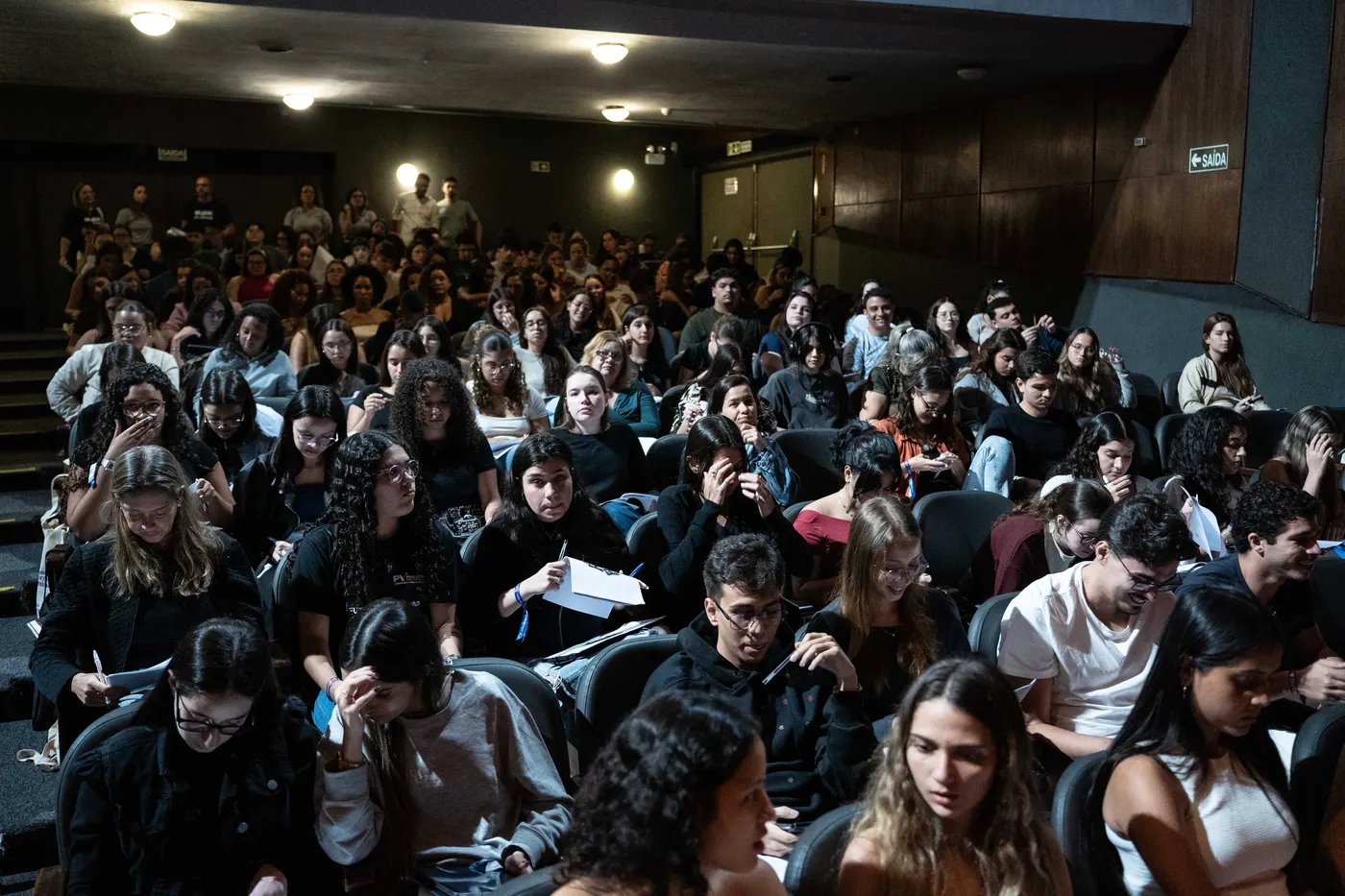 Auditório cheio, com os alunos segurando o material do evento