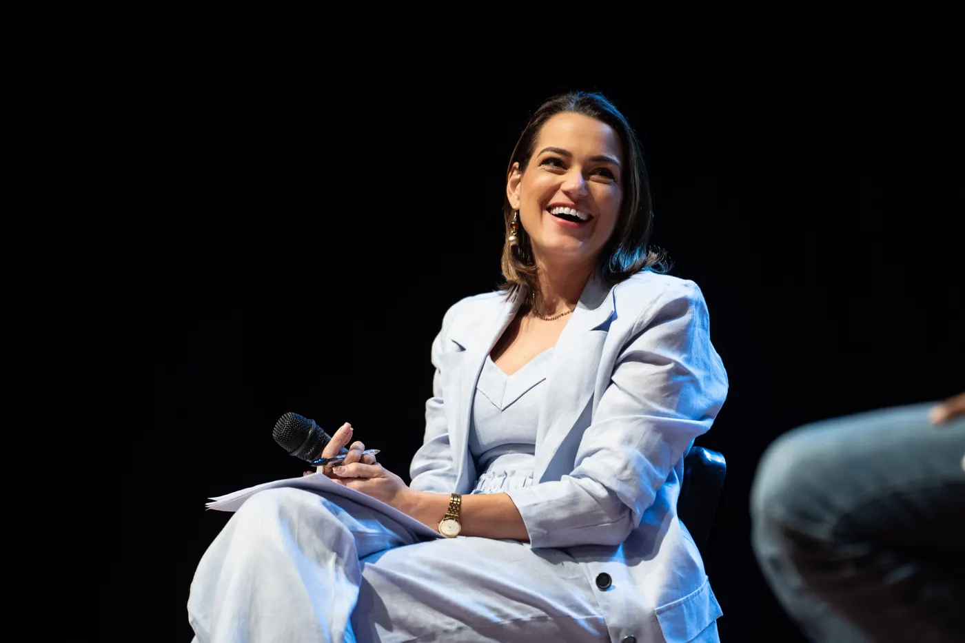Professora Milla sentada no palco, sorrindo durante a discussão